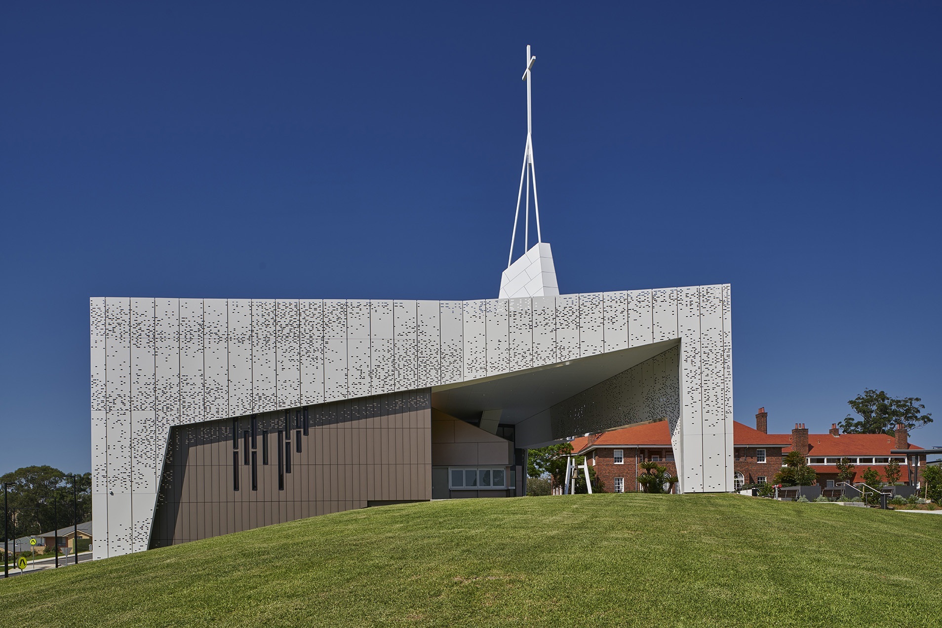 Moderne Architektur mit weißer Fassade und Kreuzspitze, umgeben von grünen Rasenflächen unter blauem Himmel