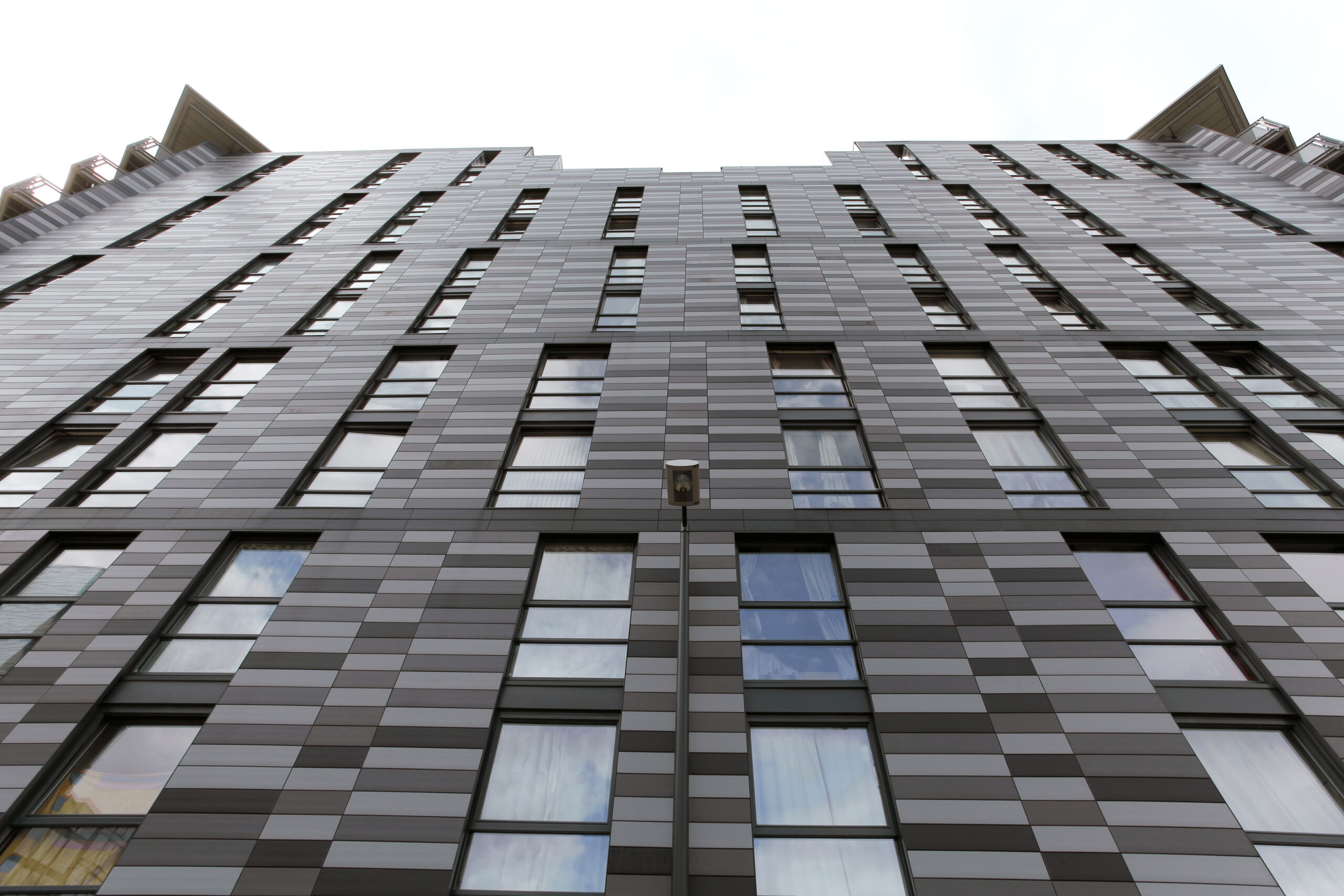 Moderne Wohngebäude im Quartermile-Viertel mit grauen Keramikpaneelen und zahlreichen Fenstern, die eine abwechslungsreiche Fassade bilden, aus der Perspektive von unten nach oben fotografiert