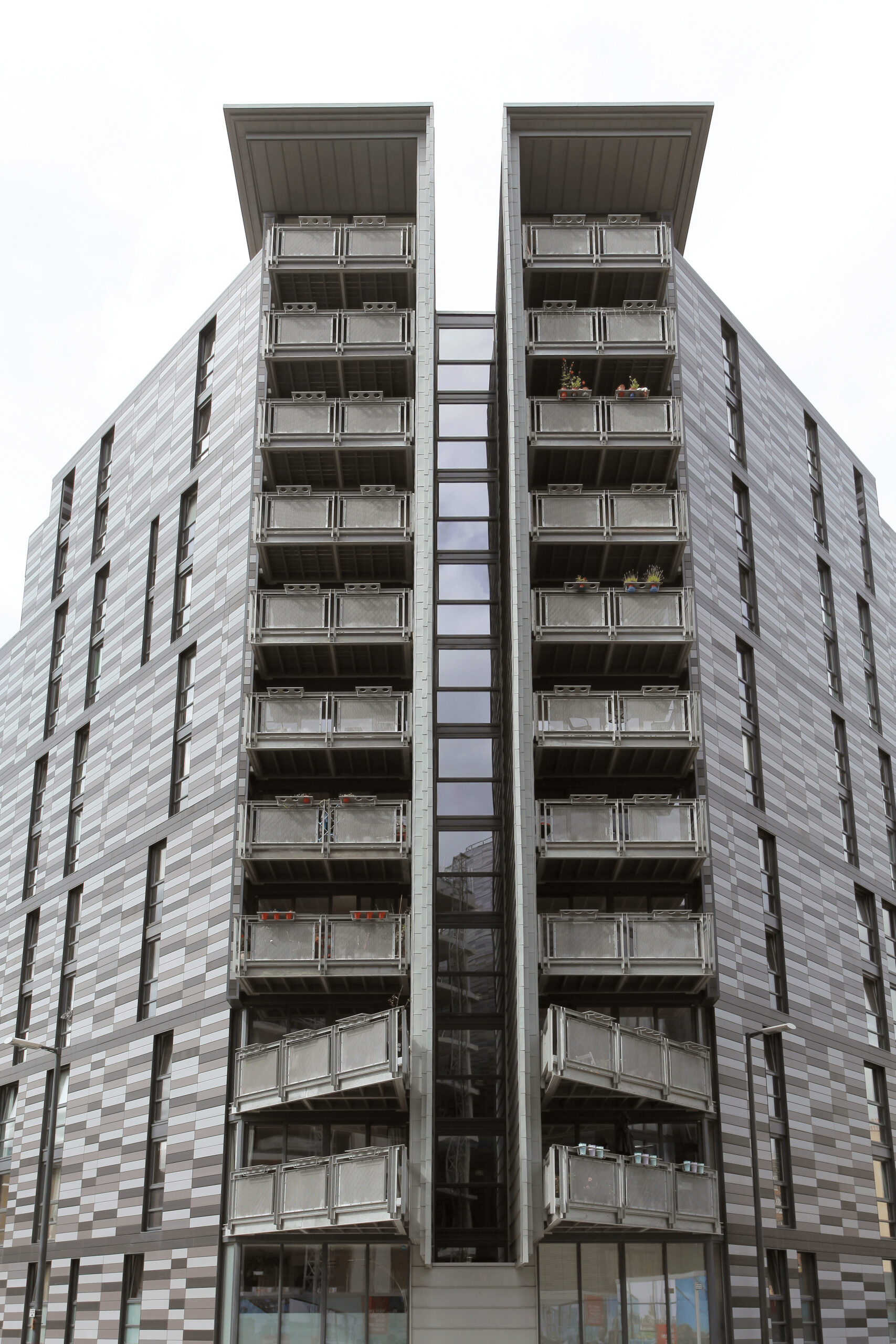 Moderne Wohngebäude im Quartermile-Viertel mit grauen Keramikpaneelen und Balkonen, die eine zentrale Glasfassade flankieren