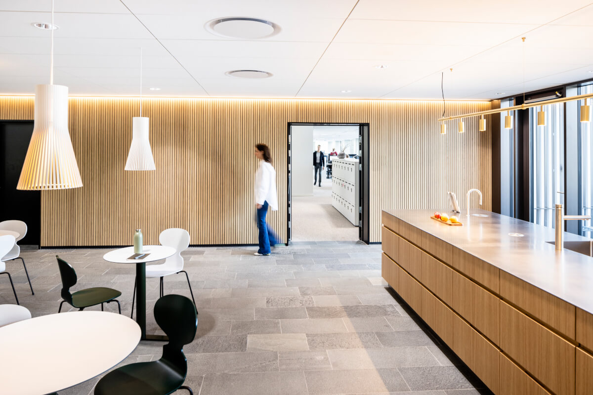 Modern and spacious public kitchen in Velliv Ballerup office, Denmark, featuring sleek white cabinets, stainless steel appliances, and a large central island with seating for colleagues to gather and socialize.