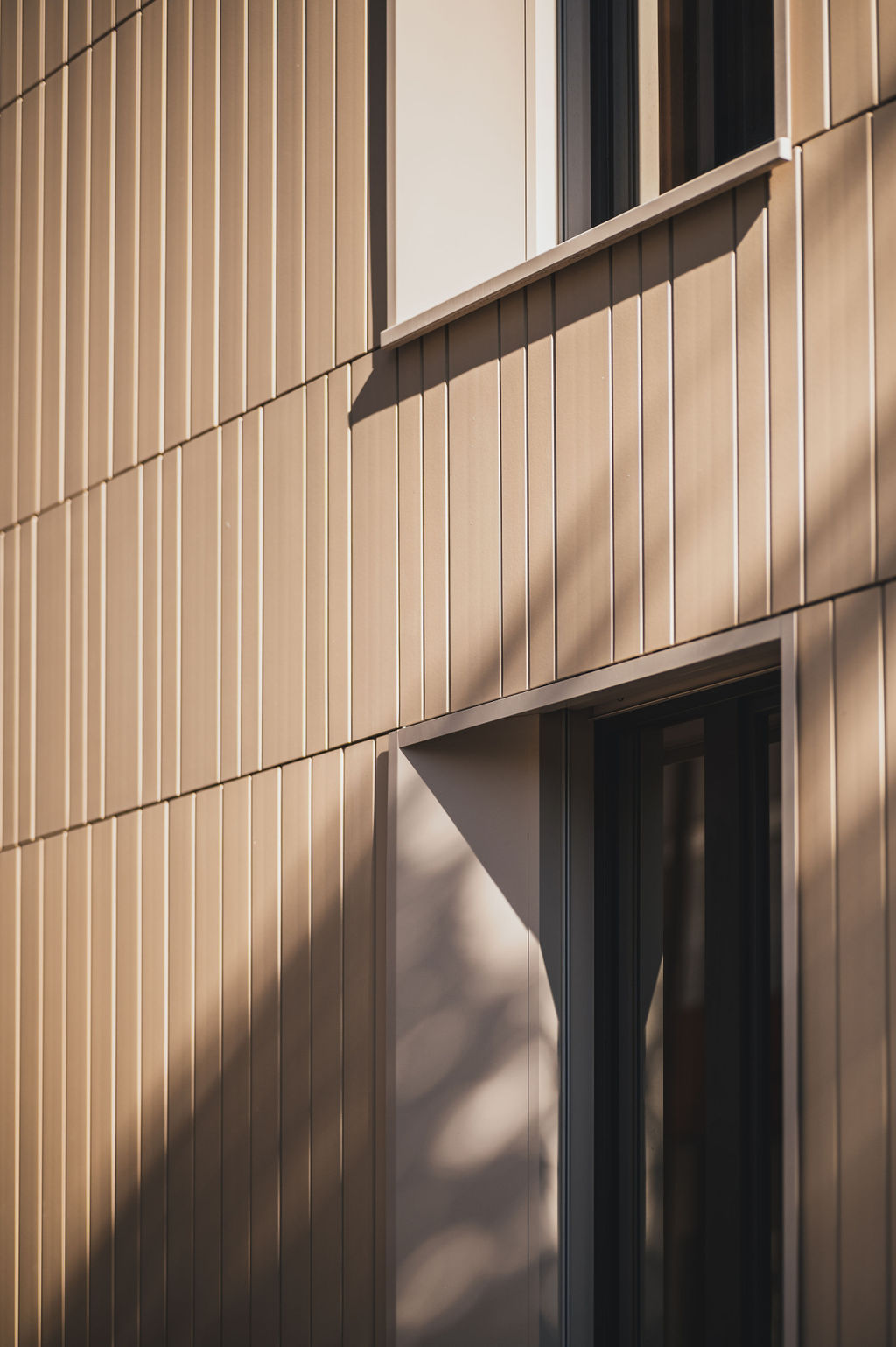 Detailaufnahme der Keramikfassade des Baerahus in Feldkirch mit vertikalen Linien und Fenstern, die von Sonnenlicht und Schatten beleuchtet werden