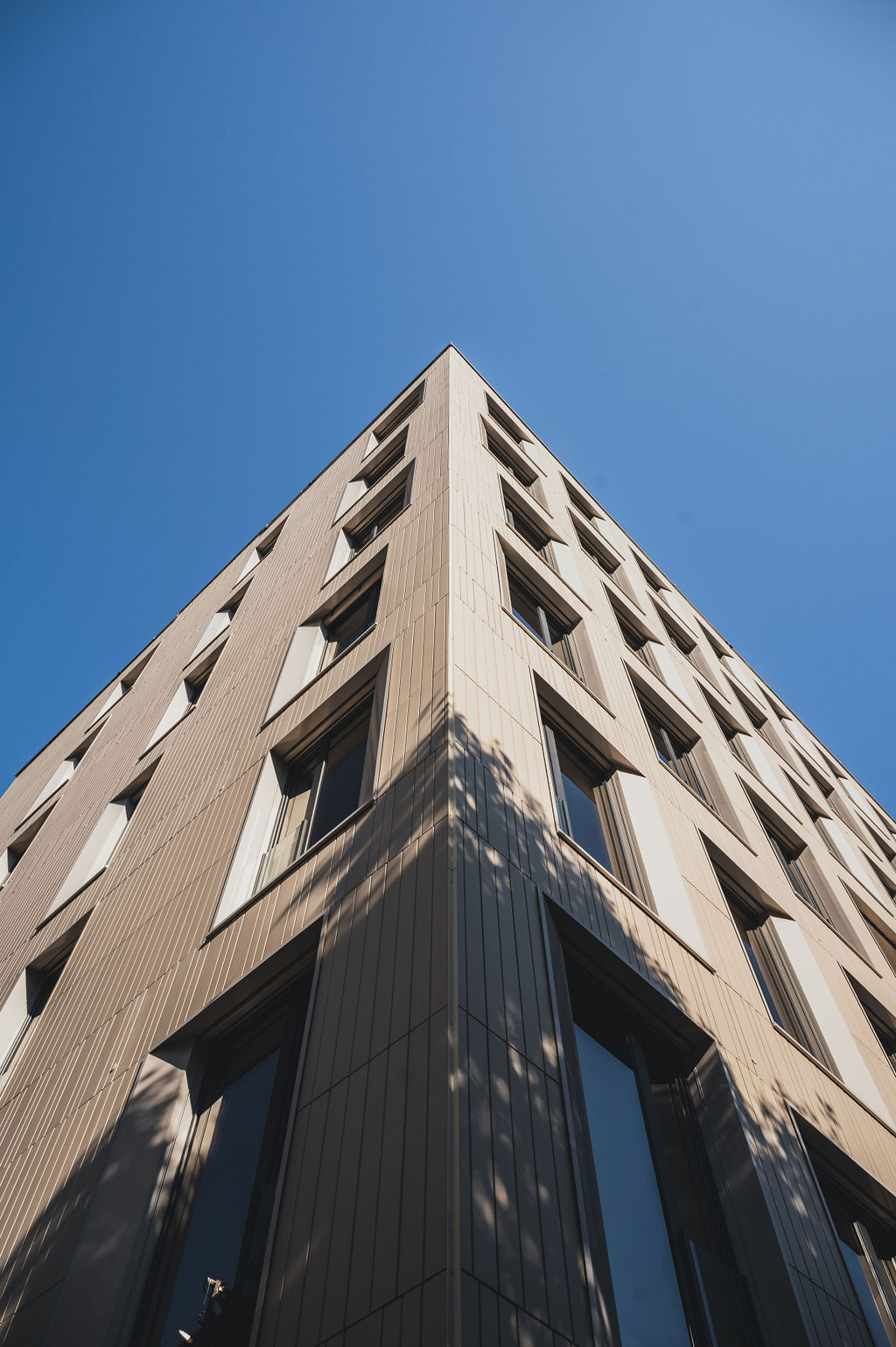 Keramikfassade des Baerahus in Feldkirch mit vertikalen Linien und großen Fenstern, fotografiert aus einem niedrigen Winkel gegen den blauen Himmel