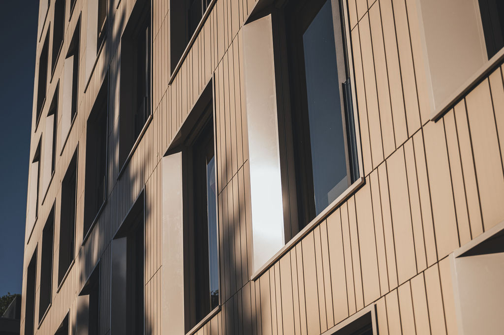 Keramikfassade des Baerahus in Feldkirch mit vertikalen Linien und großen Fenstern im Sonnenlicht