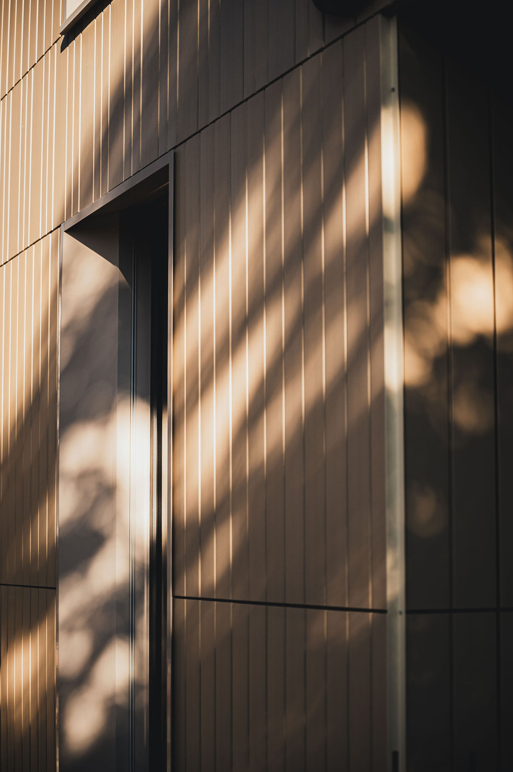 Detailaufnahme der Keramikfassade des Baerahus in Feldkirch mit vertikalen Linien und Schatten von Bäumen