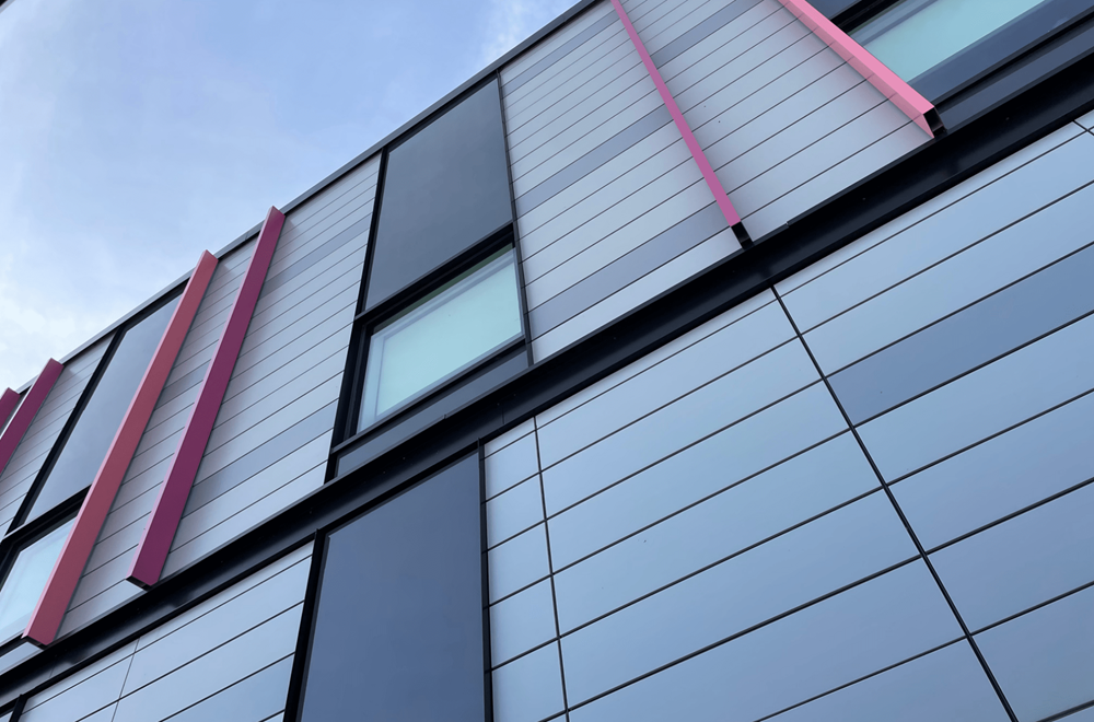 Fassade des modernen Bayers Lake Outpatient Centers mit vertikalen roten Akzenten und reflektierenden Glasflächen unter blauem Himmel.
