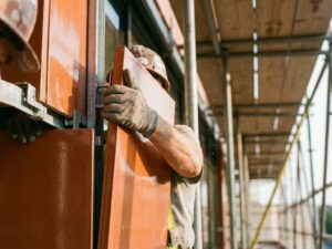 Construction worker installing terracotta panel on building facade with metal brackets and scaffolding visible