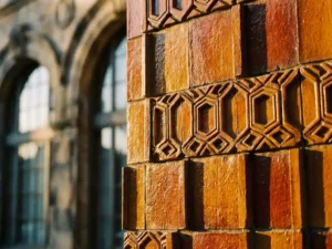 Terracotta ceramic facade tiles with geometric patterns in warm amber tones, dramatic shadows highlighting textural depth