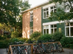 Nachhaltige Schulgebäude-Fassade mit Keramikfliesen in Terrakotta und Grün, Fahrradständer mit Schülerrädern im Vordergrund, goldenes Nachmittagslicht.